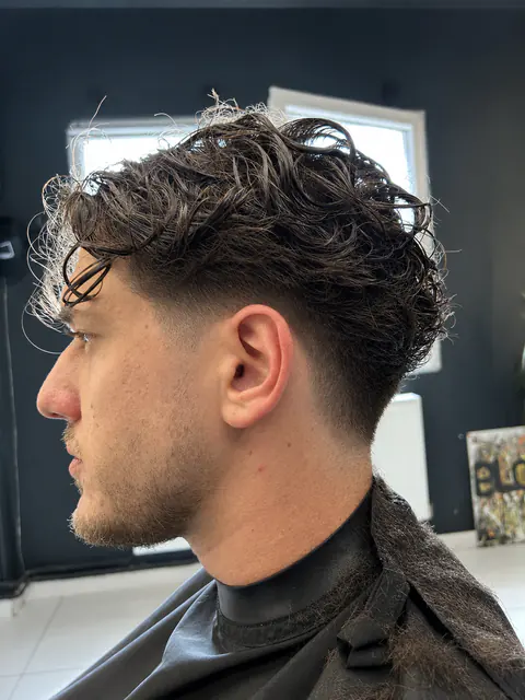 Férfi hajvágás természetes fürtökkel felül és tiszta fade átmenettel oldalt, profilból