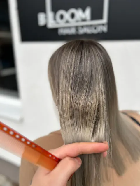 Sima, hamvas bronde haj fésülése a BLOOM Hair Salon felirata előtt