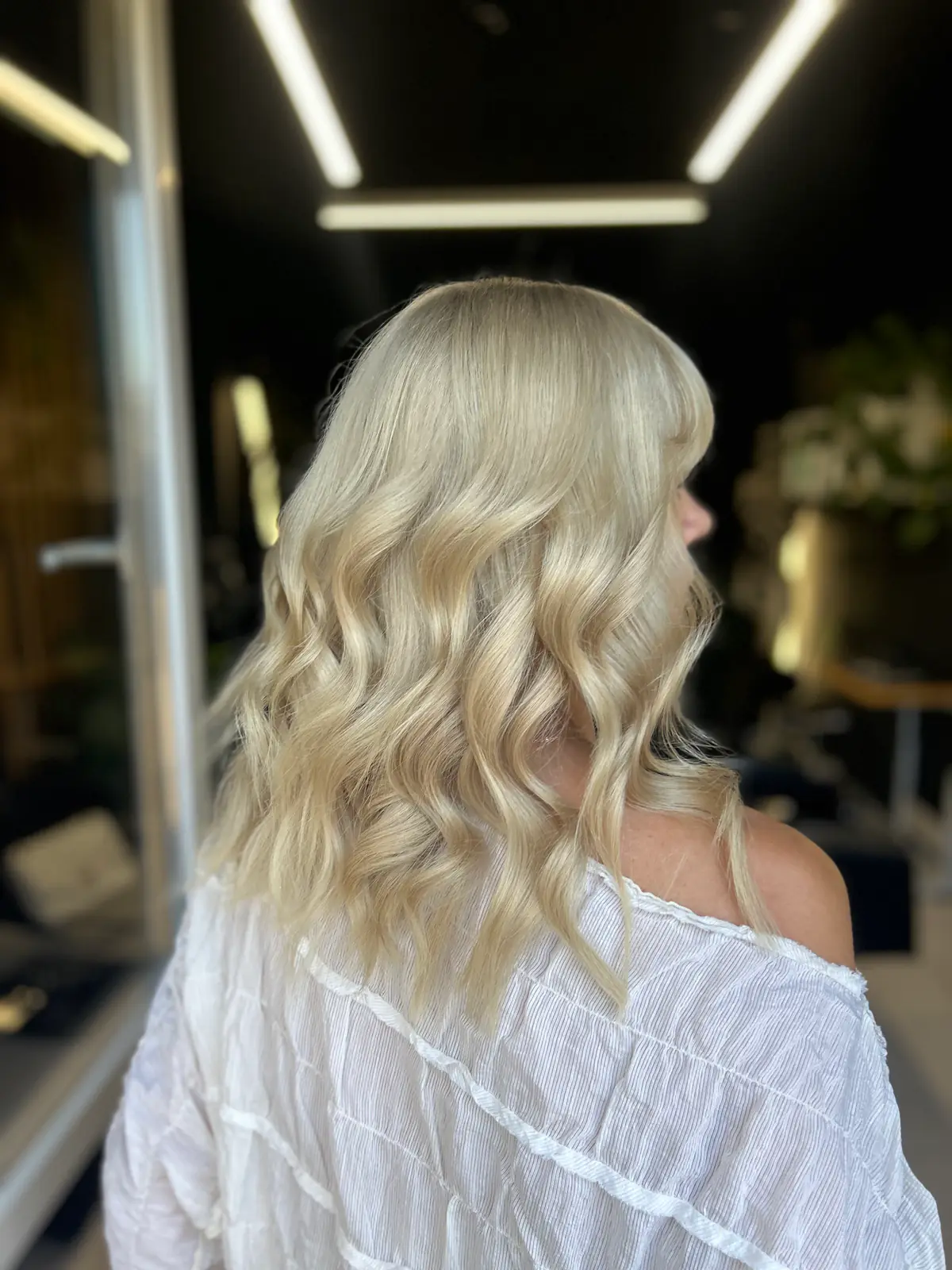 Clientă în bluză albă, cu păr blond șampanie aranjat în bucle moi, în salon