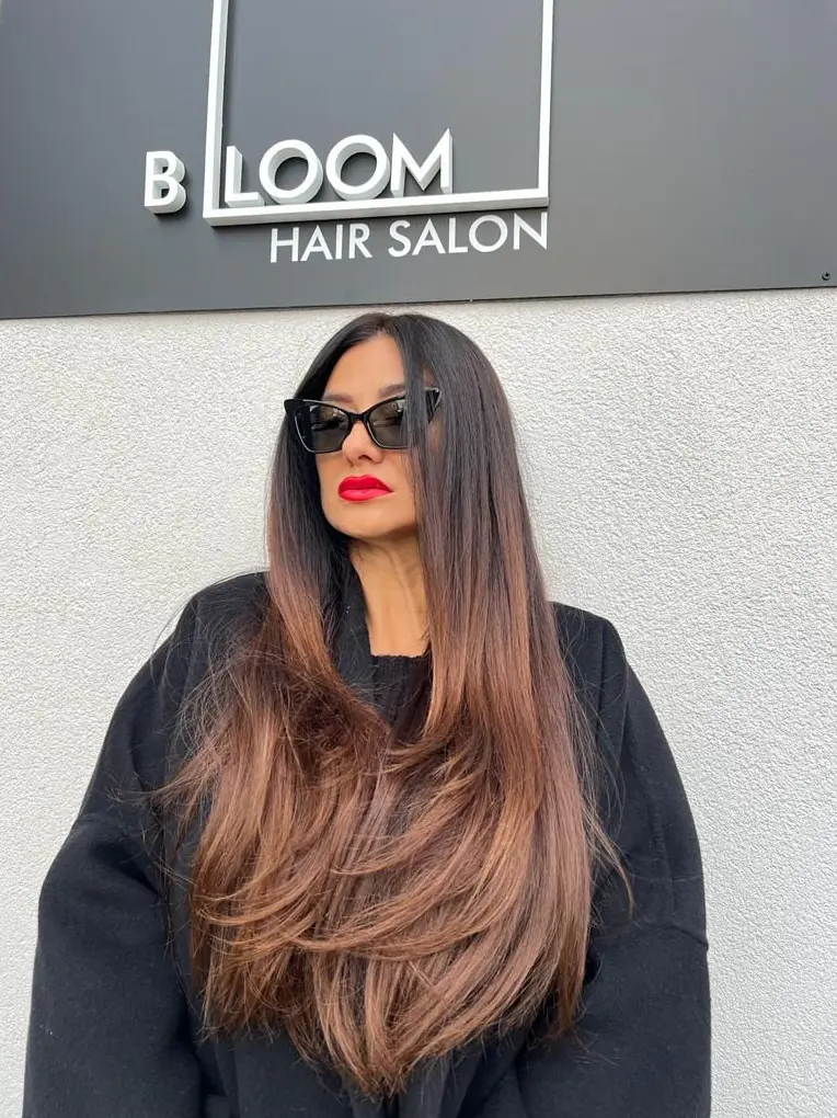 Client in sunglasses under the BLOOM Hair Salon sign in Târgu-Mureș, with long layered mocha ombré hair